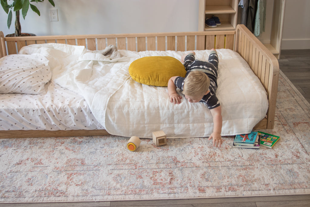 A little boy lays on a twin floor bed with two headboards and one full side