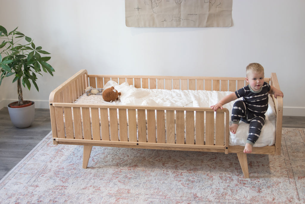 A small child sits on the edge of the platform oak bed with two headboards, a full side rail and a 3/4 rail with legs
