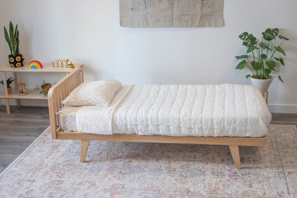 The twin floor bed frame with one headboard and legs with a white bedspread