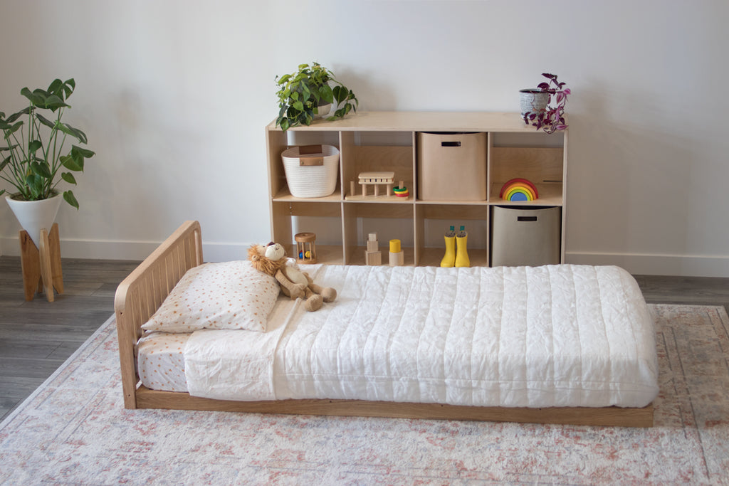 The oak montessori floor bed with one headboard and a six cube shelf in the background