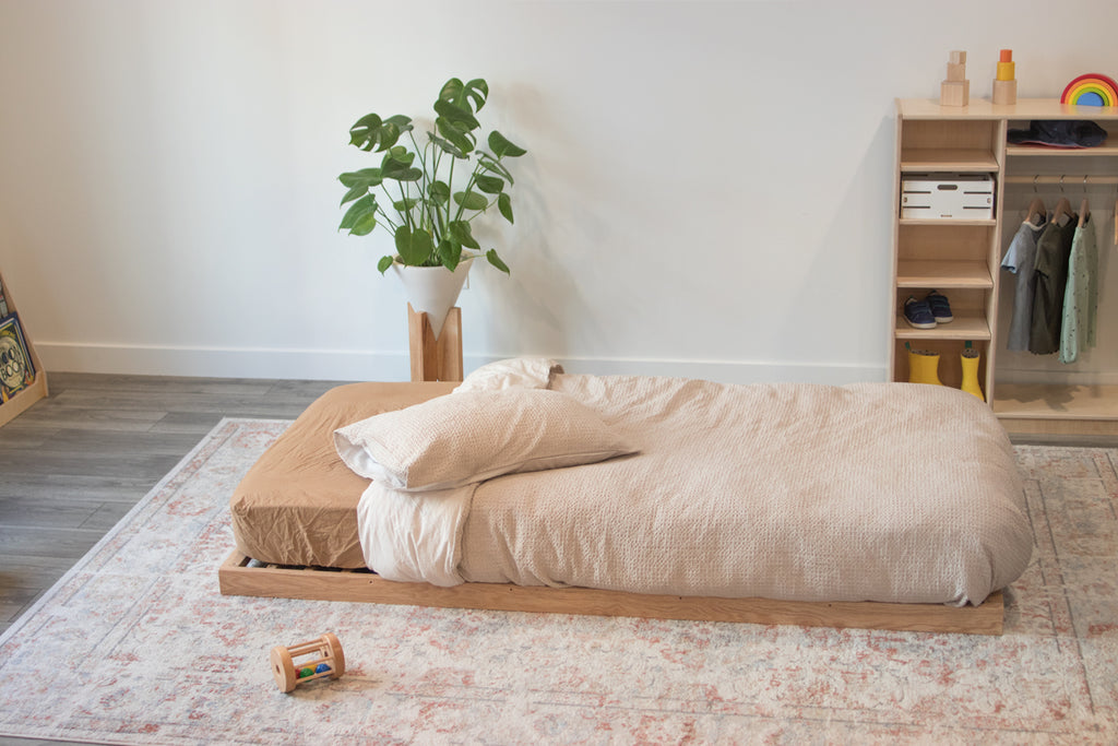 An oak floor bed frame with a mattress on top and a child's wardrobe in the background