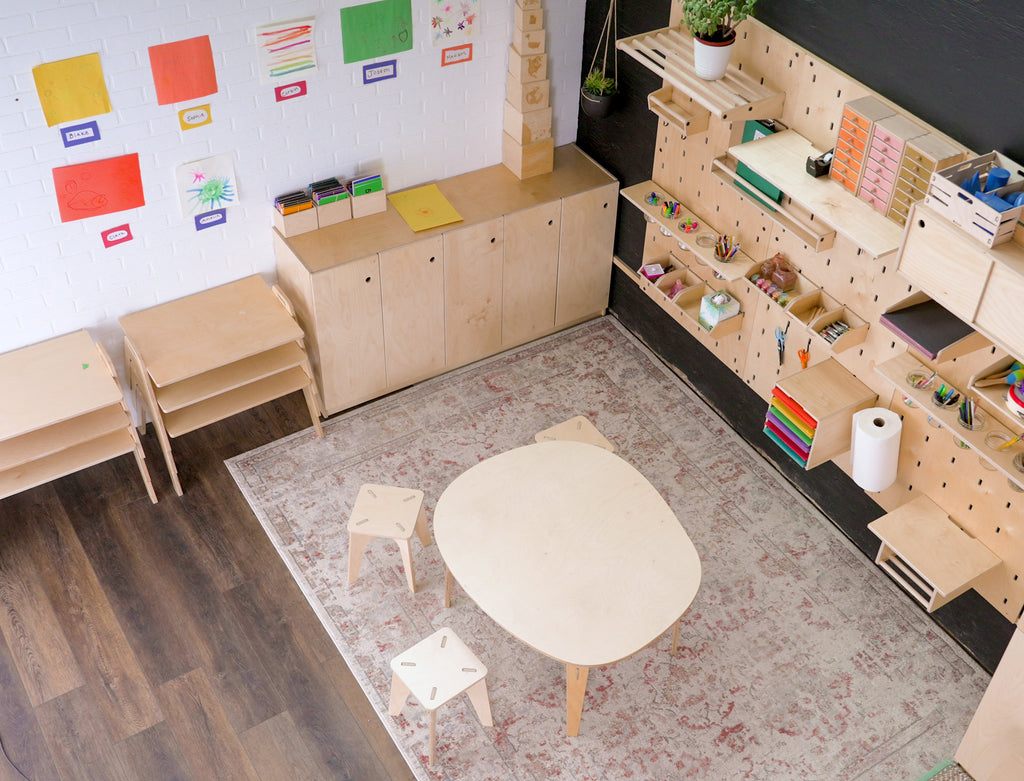 Bird's eye view of a Wood Grain Laminate Pebble table with 3 children's stools in a prepared Montessori learning environment.