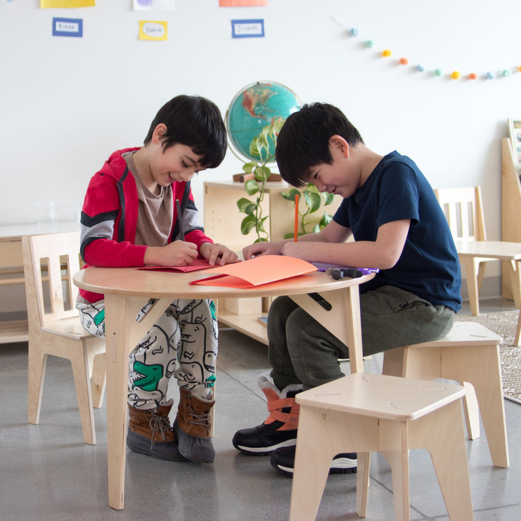 Two boys drawing on colored paper on a round table. 
