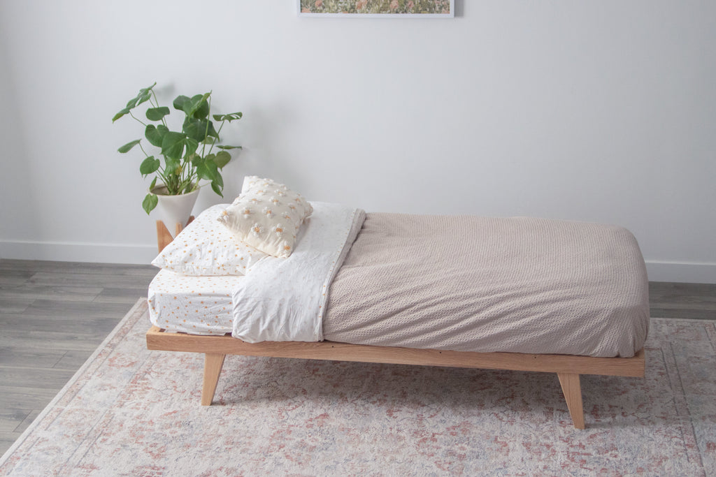 The oak bed frame with legs and a mattress on top 